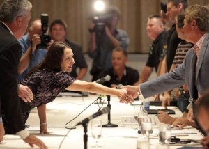two people shaking hands across a table with cameras taking pictures